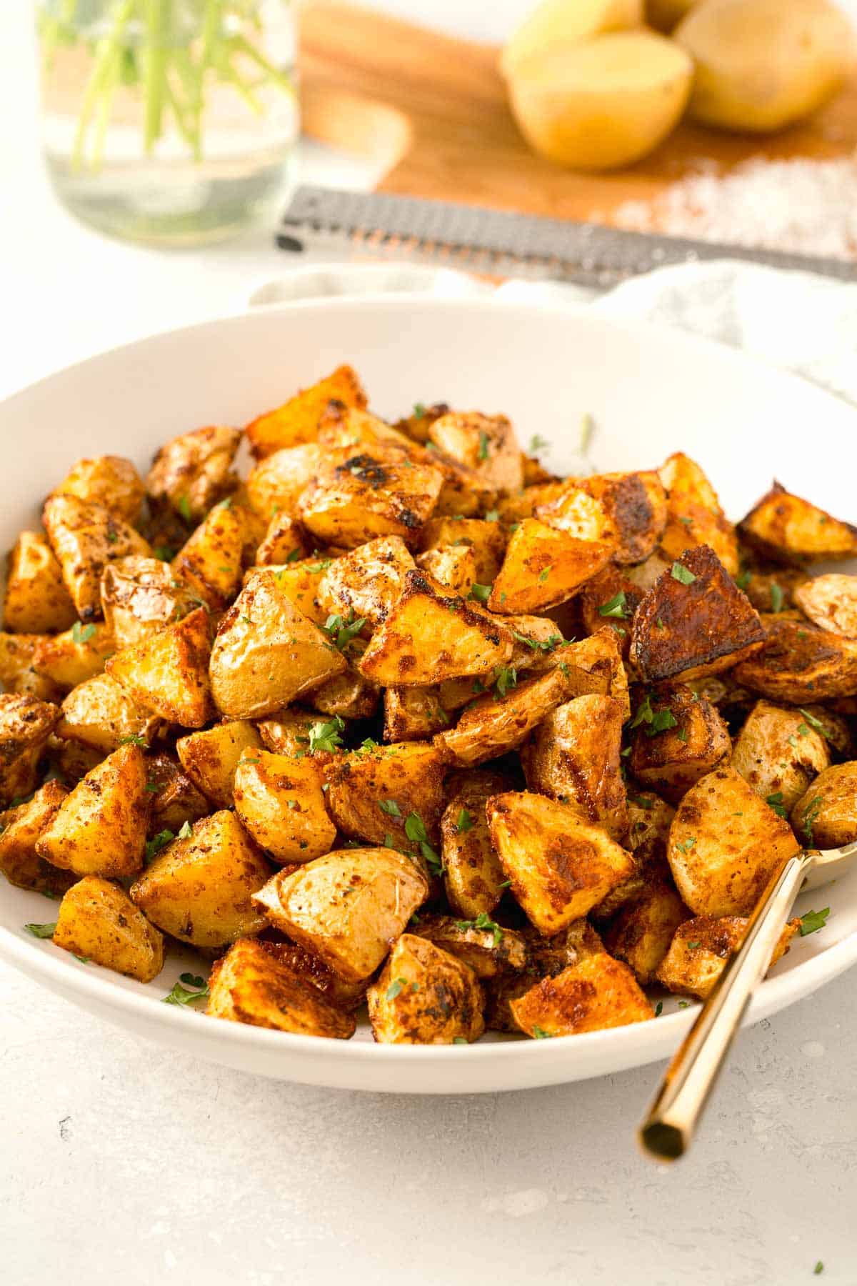 roasted parmesan potatoes in a large white bowl with gold metal spoon