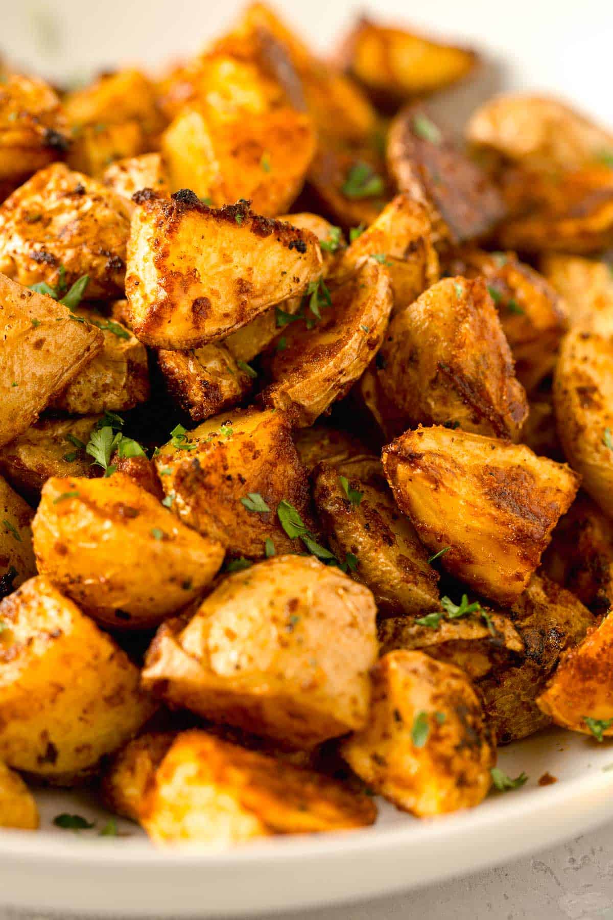 large amount of roasted parmesan potatoes in a large white bowl with fresh parsley sprinkled on top