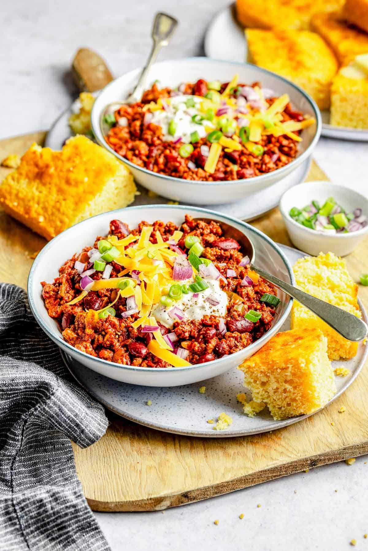 2 bowls of slow cooker chili loaded with toppings.