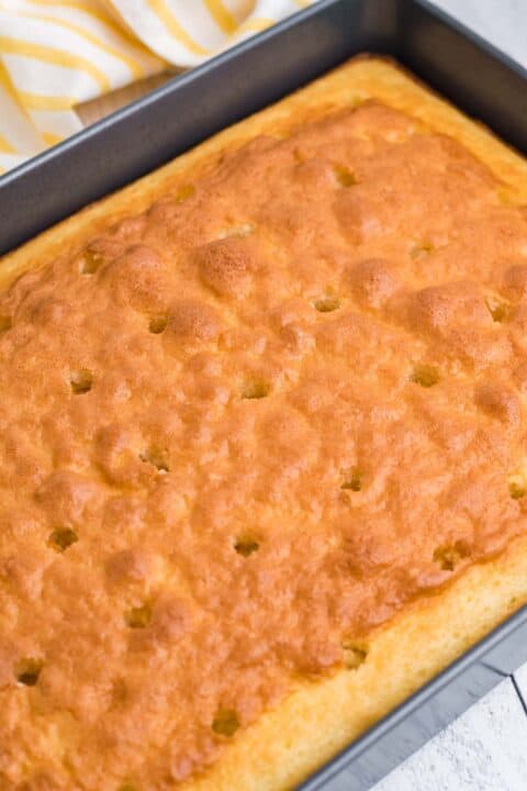 Holes are poked across the top of a baked white cake.