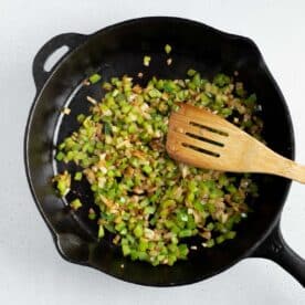 green onions and onions in a cast iron skillet with a wooden spoon