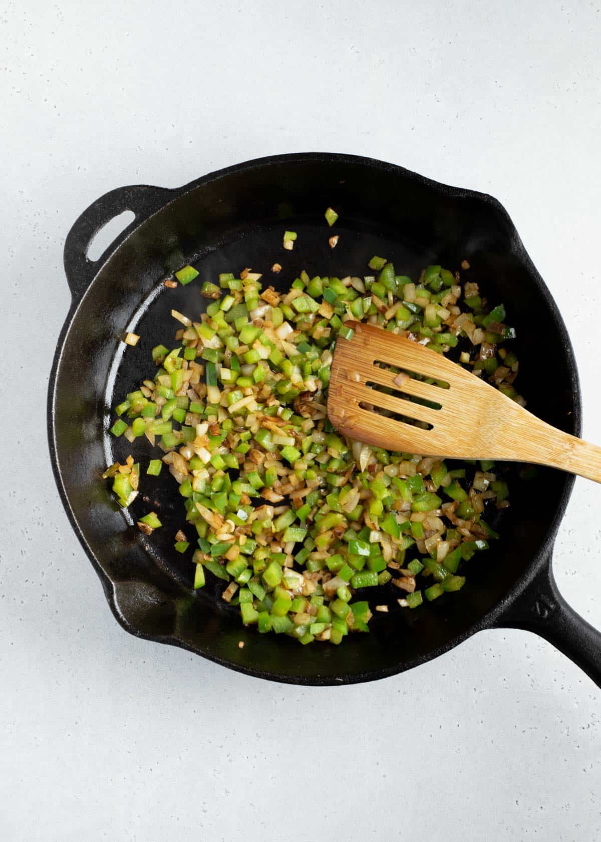 green onions and onions in a cast iron skillet with a wooden spoon