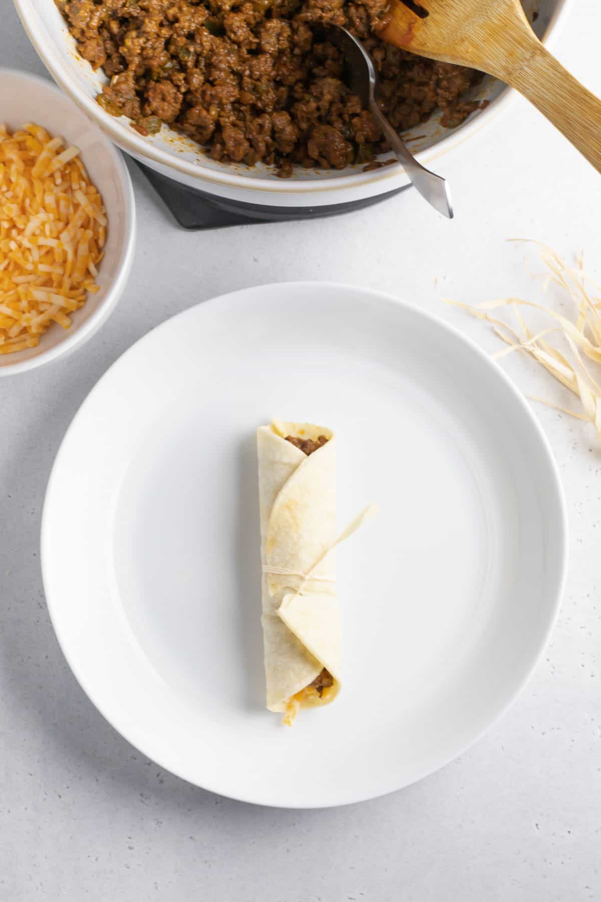 beef taquito rolled up and tied with a corn husk string on a white plate