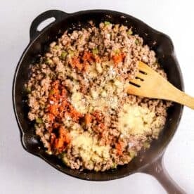 ground beef mixture with green bell peppers in a cast iron skillet with seasonings sprinkled on top