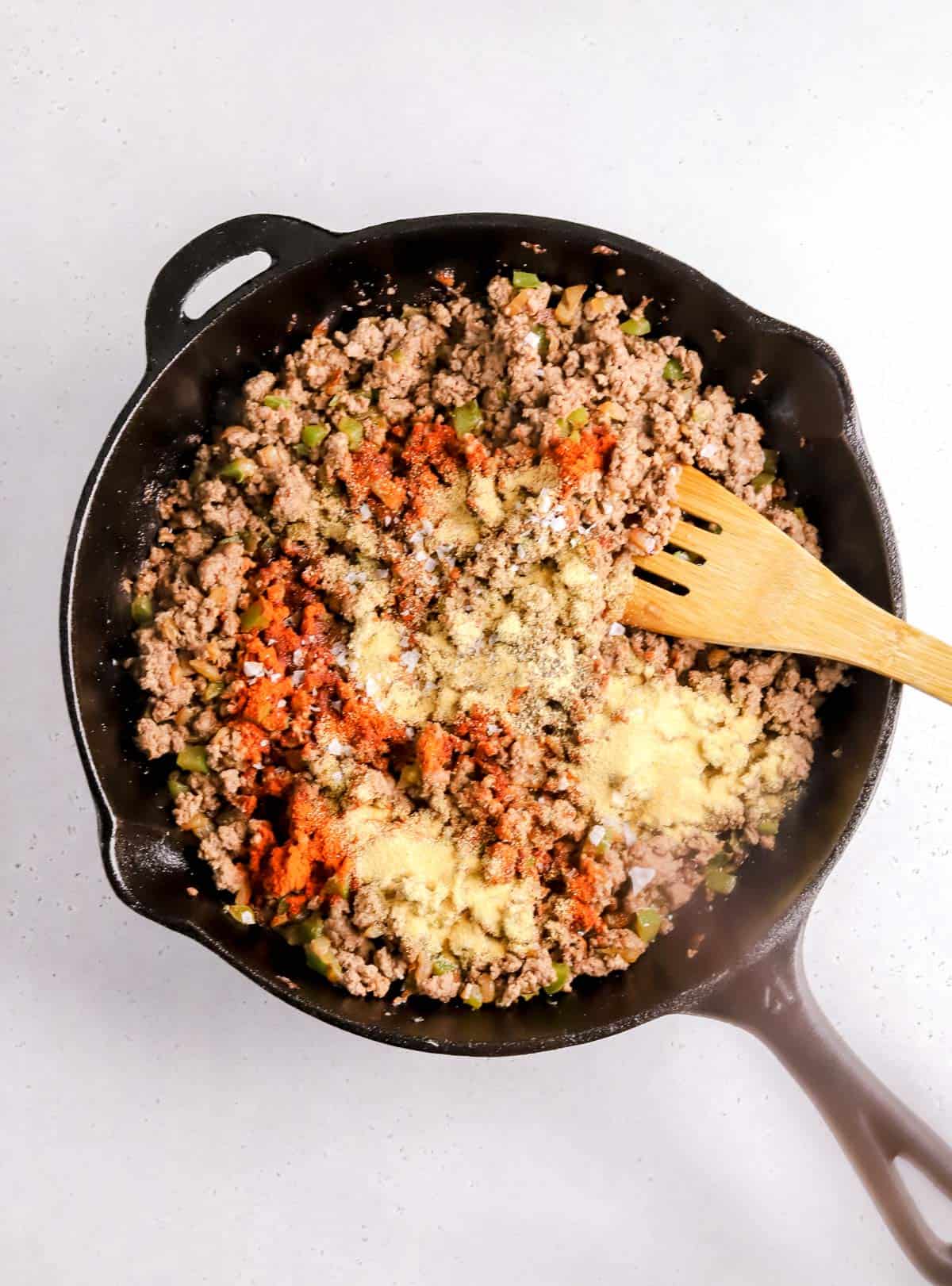 ground beef mixture with green bell peppers in a cast iron skillet with seasonings sprinkled on top