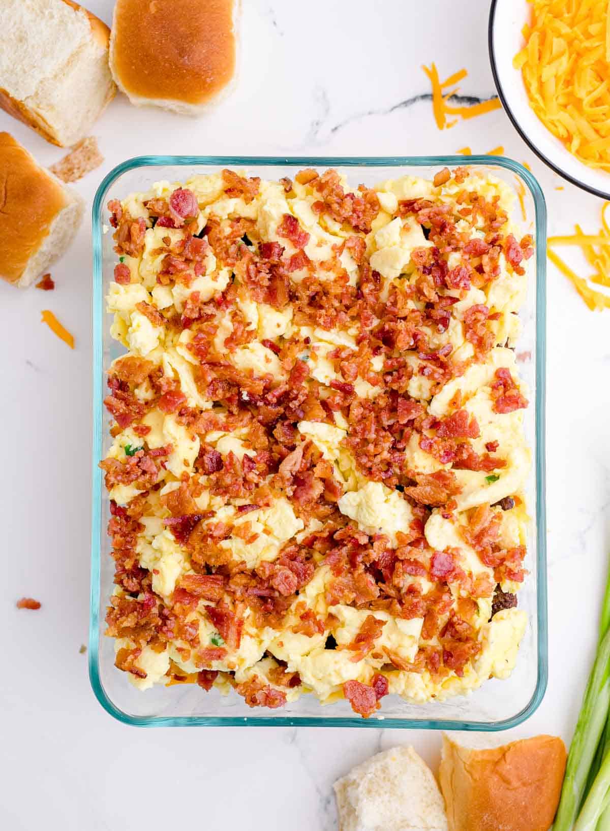 crumbled bacon spread on top of scrambled eggs in a glass baking dish