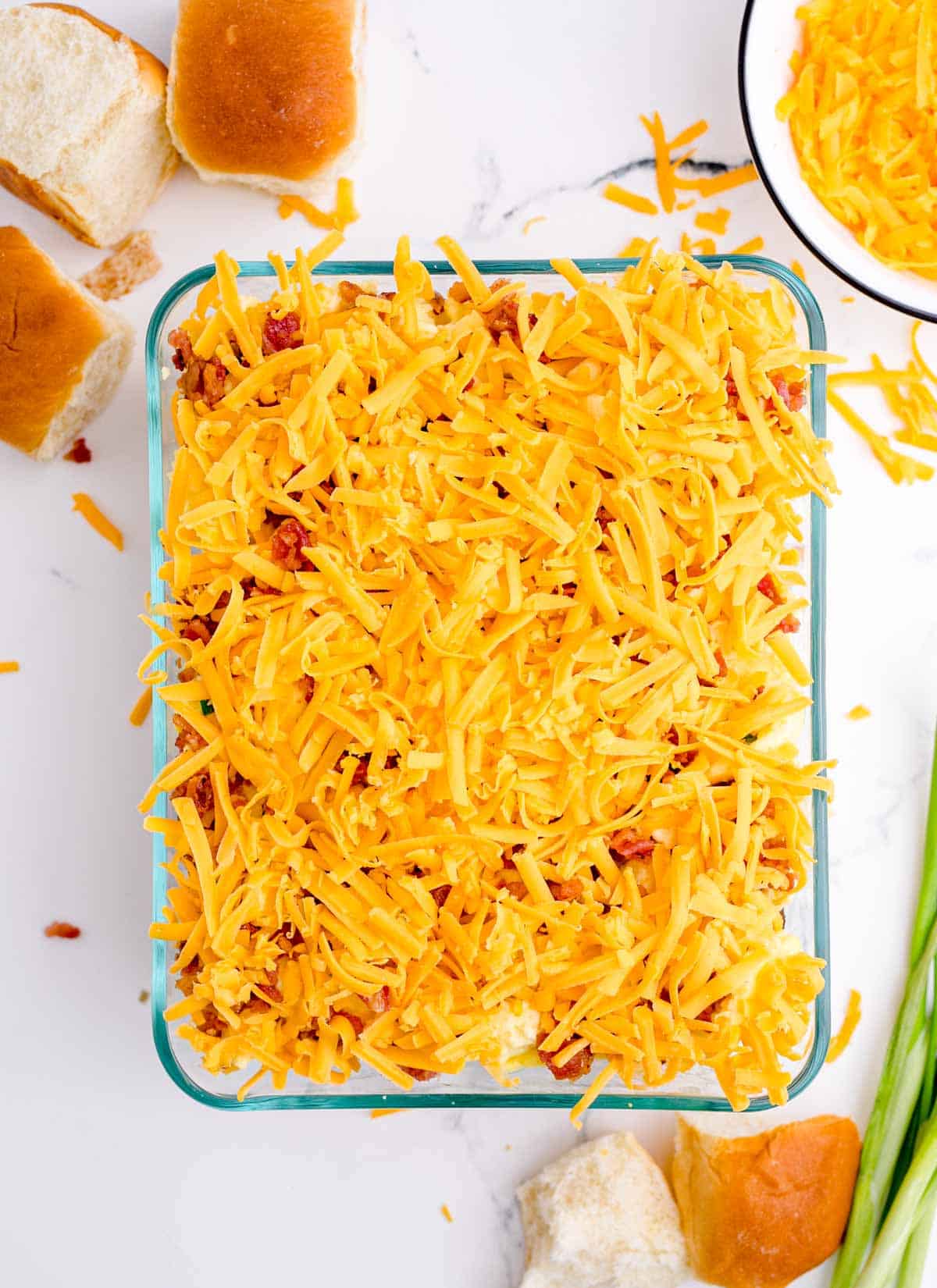 shredded cheddar cheese added on top of crumbled bacon layer in a glass baking dish