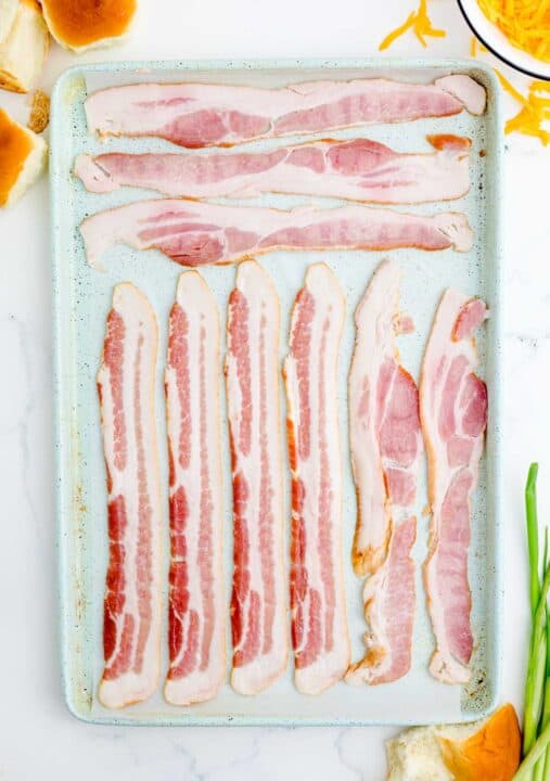 bacon individually lined up on a metal baking sheet with parchment paper