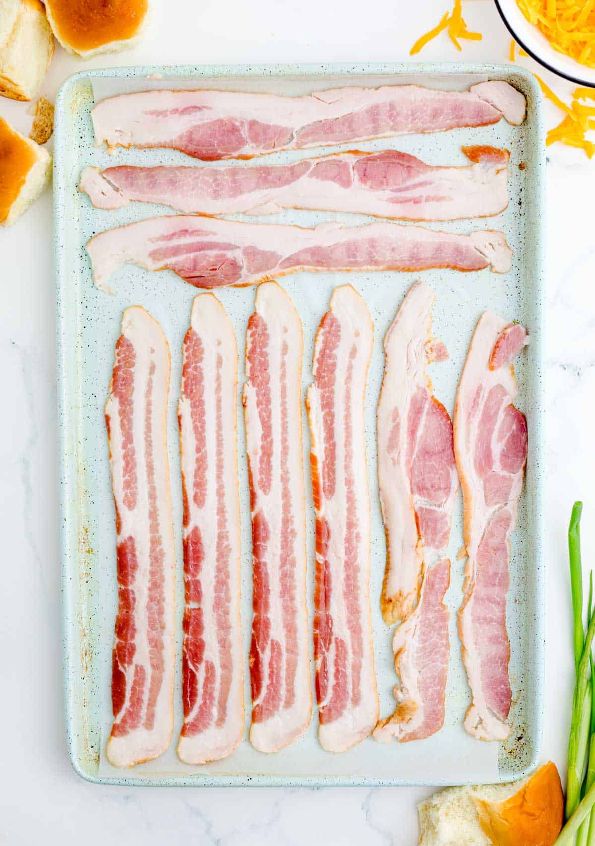 bacon individually lined up on a metal baking sheet with parchment paper