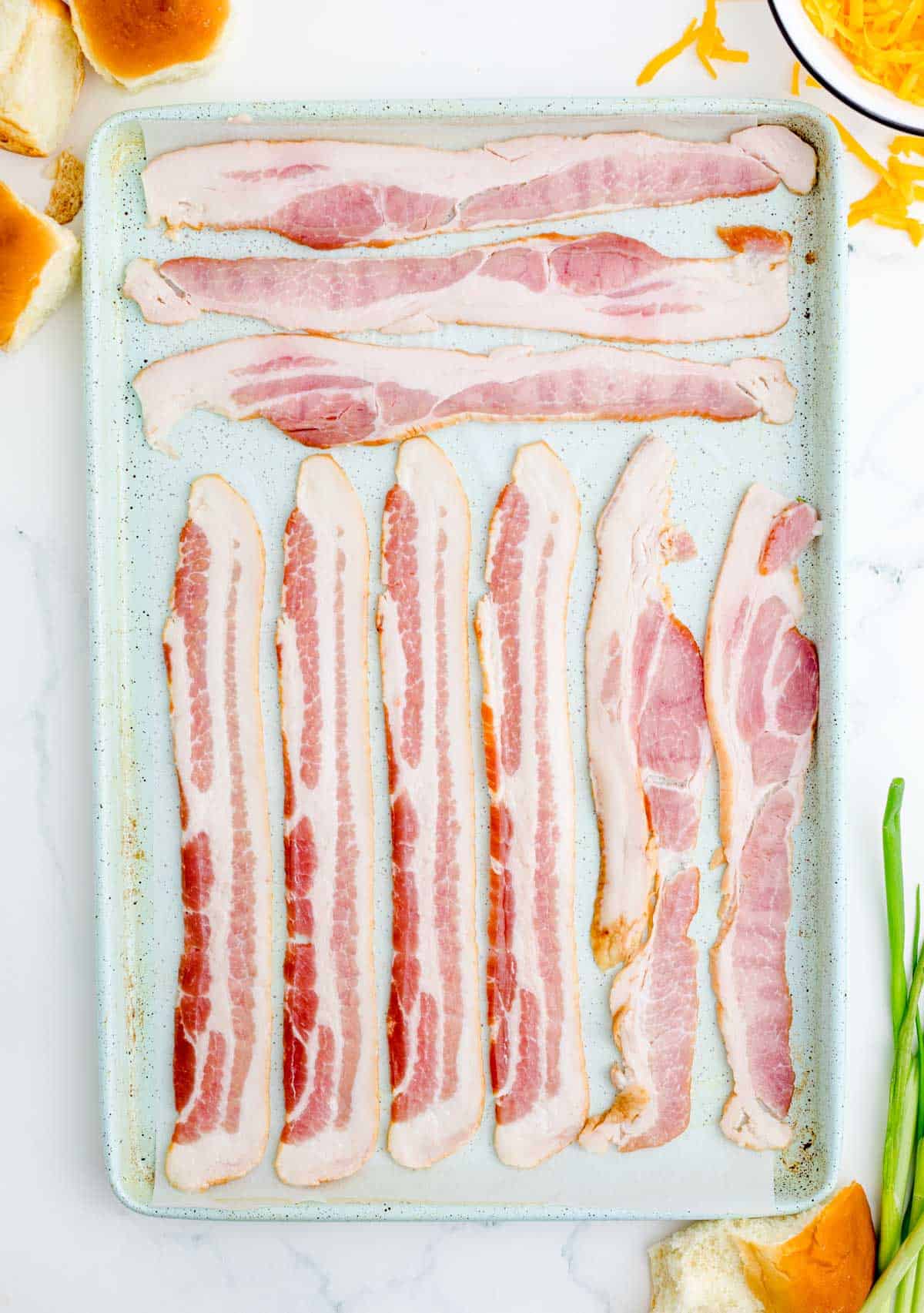 bacon individually lined up on a metal baking sheet with parchment paper