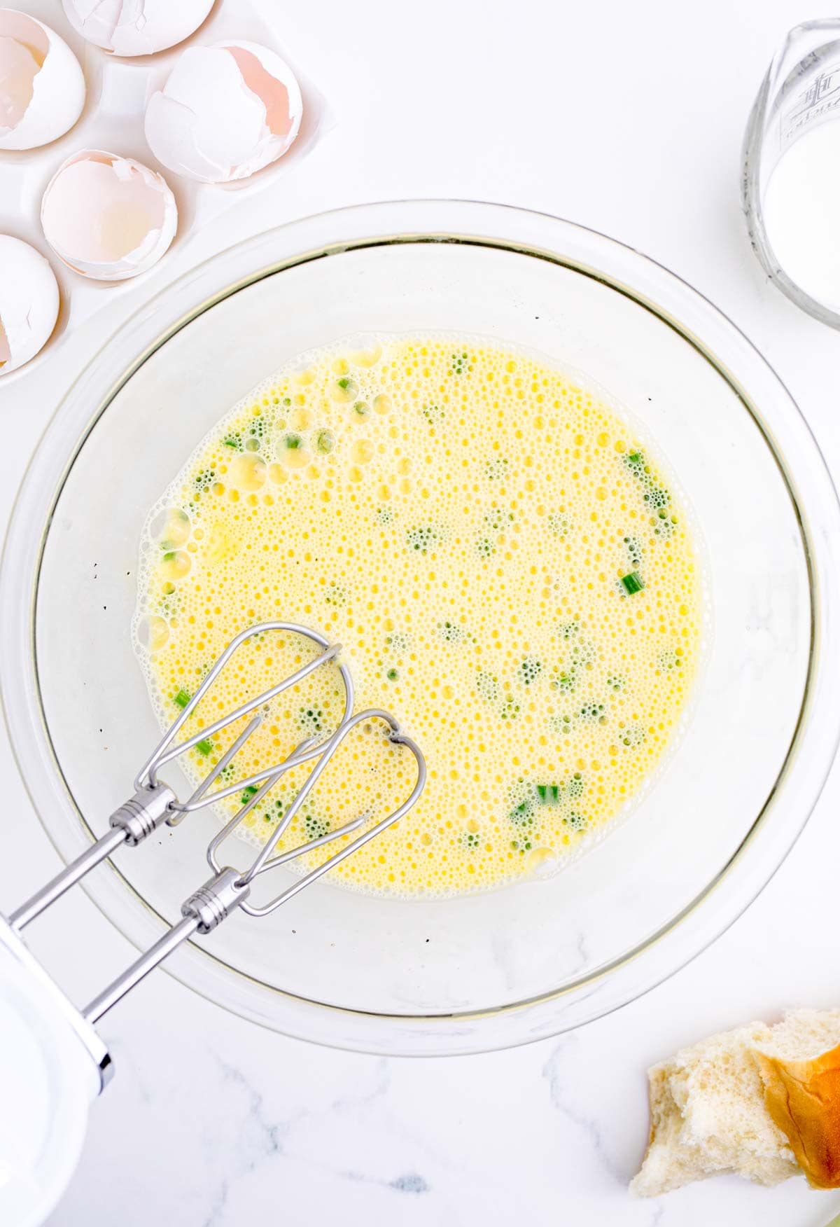 egg mixture in a clear glass bowl with green onions and an electric mixer beater in the bowl