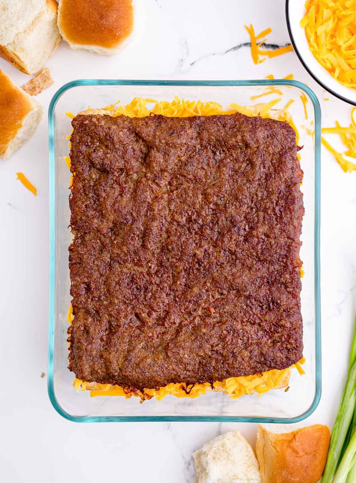 baked pork sausage square placed on top of shredded cheddar cheese in a glass baking dish