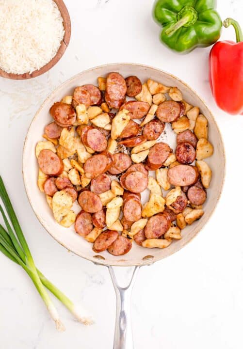 chicken and sausage cooked and browned in a white skillet