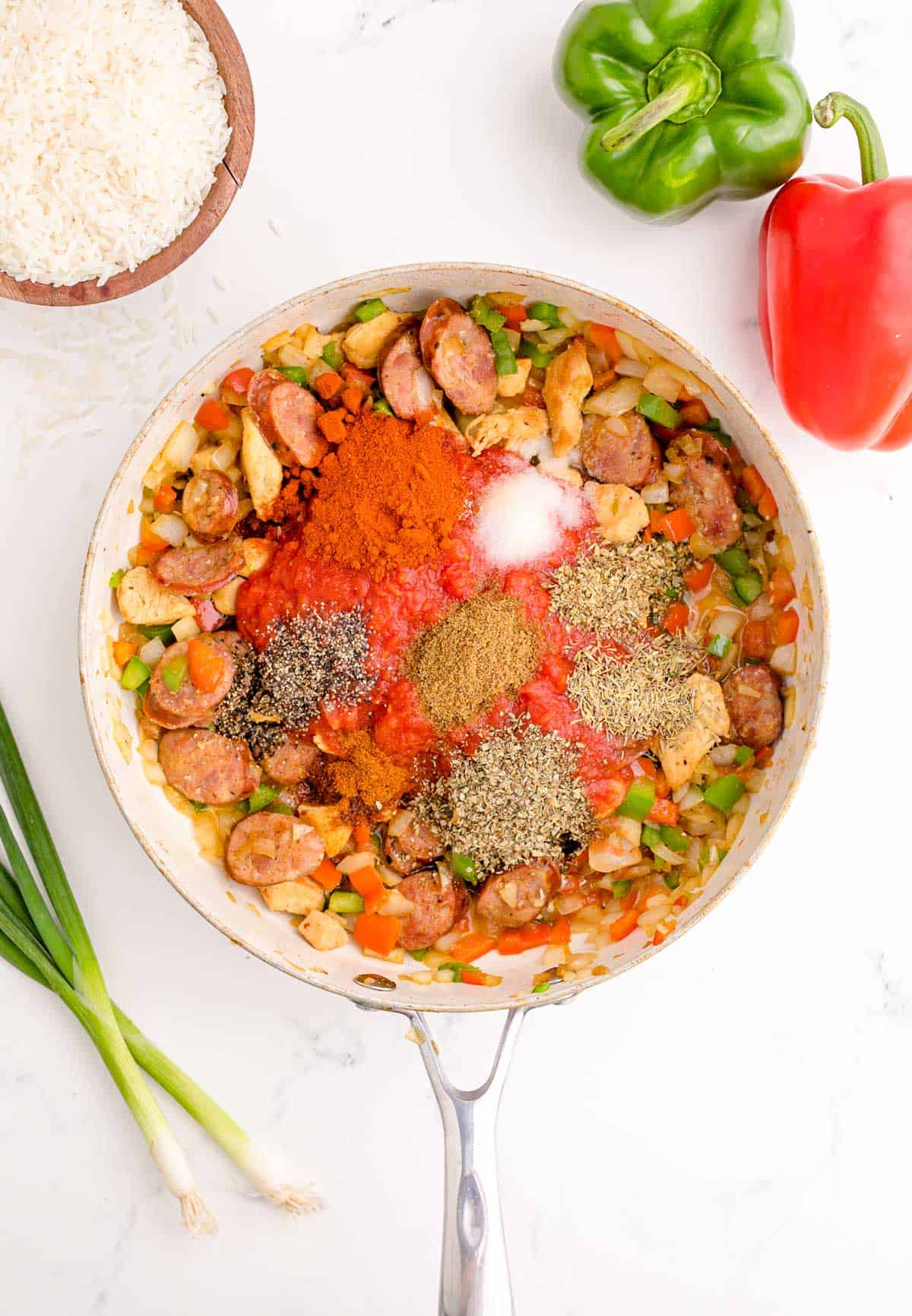 seasonings added to the skillet with chicken, vegetables, and sausage