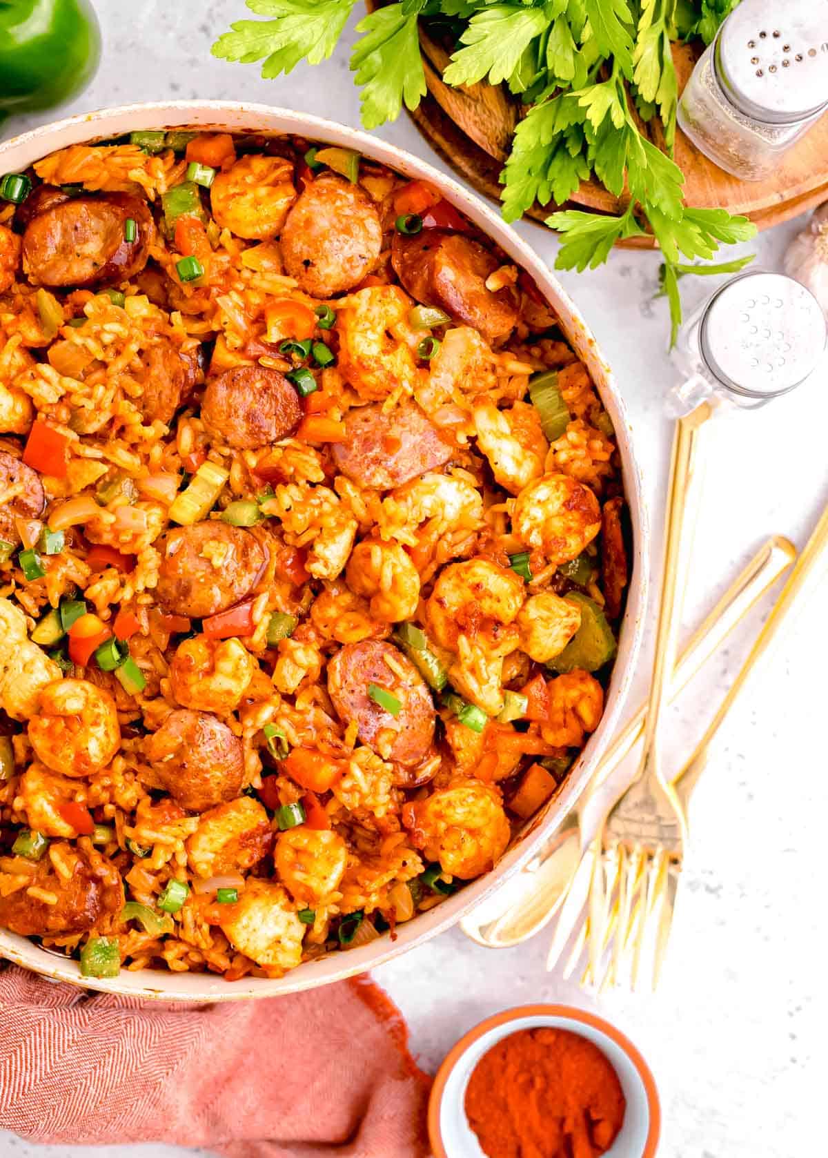 chicken and sausage jambalaya in a skillet next to gold utensils and a red linen towel
