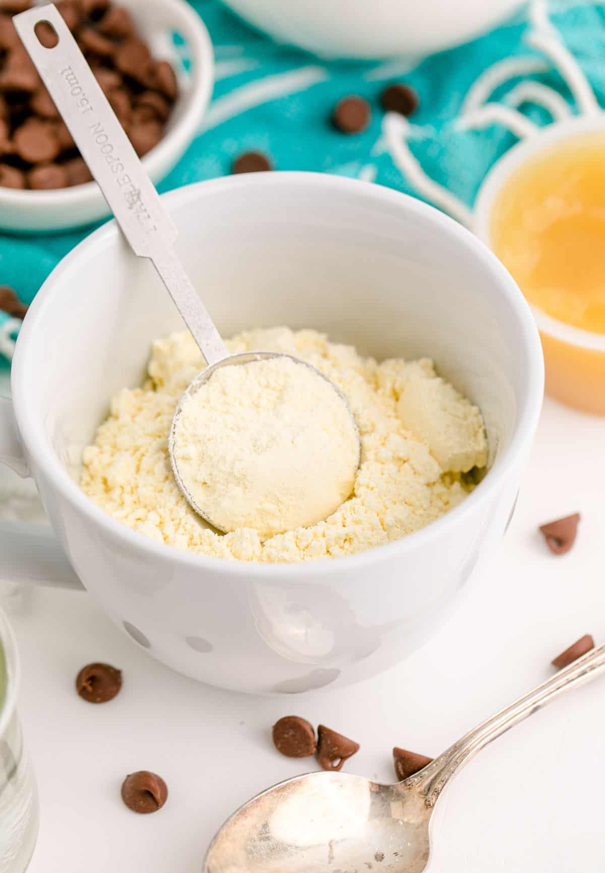 cake mix in a white mug with a tablespoon measuring spoon inside