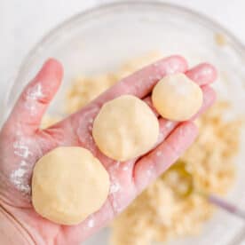 A hand is holding three balls of cookie dough.