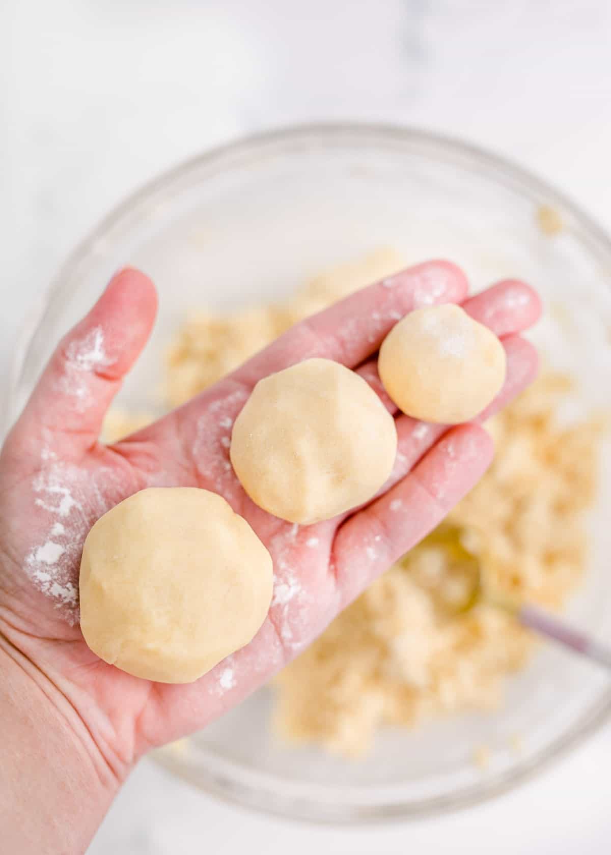 A hand is holding three balls of cookie dough.