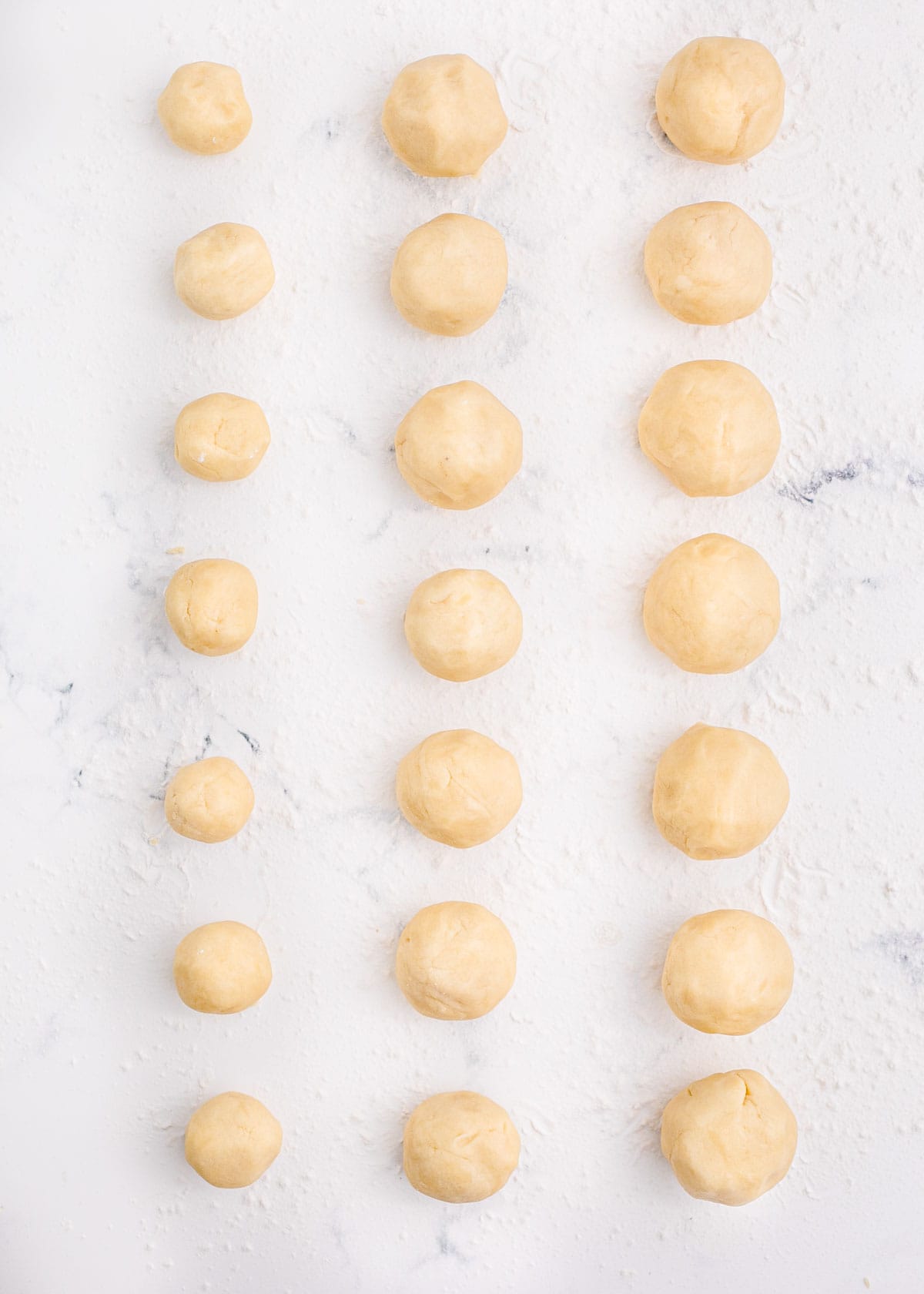 Balls of cookie dough in three different sizes are on a counter.