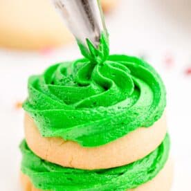 Green icing is being piped onto sugar cookies in a stack.