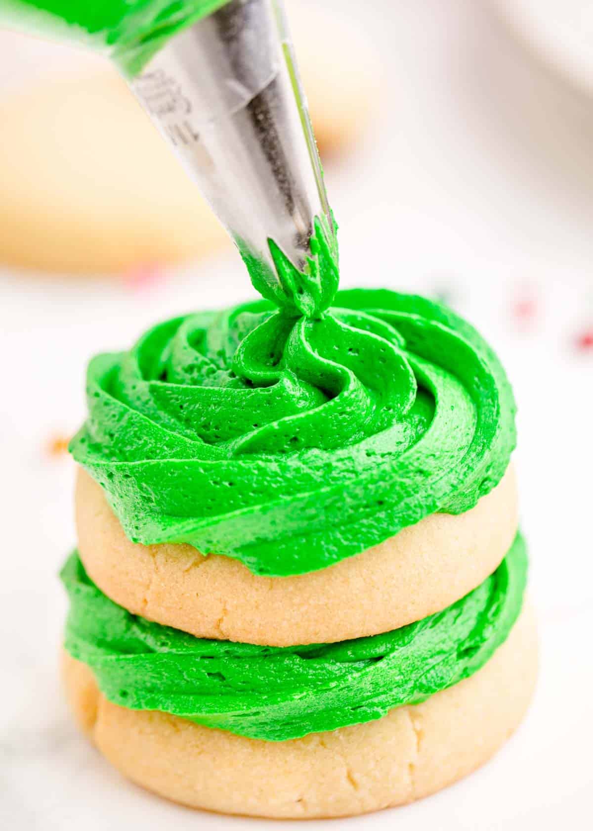 Green icing is being piped onto sugar cookies in a stack.