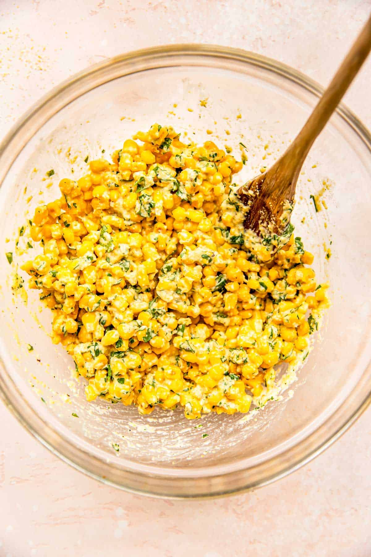 a wooden spoon in a clear bowl stirs together the corn fritter batter