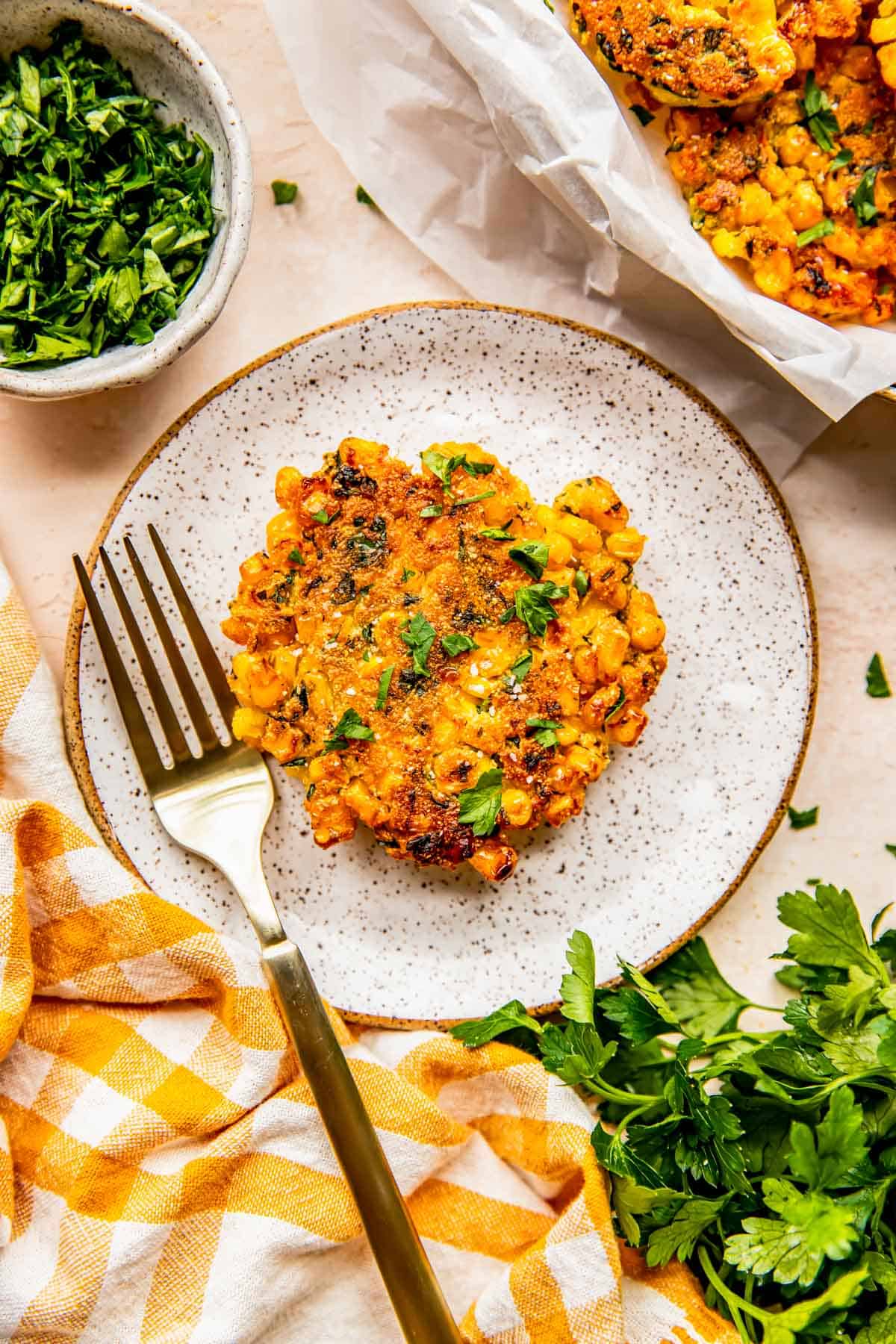 a single corn fritter on a speckled plate with a gold metal fork