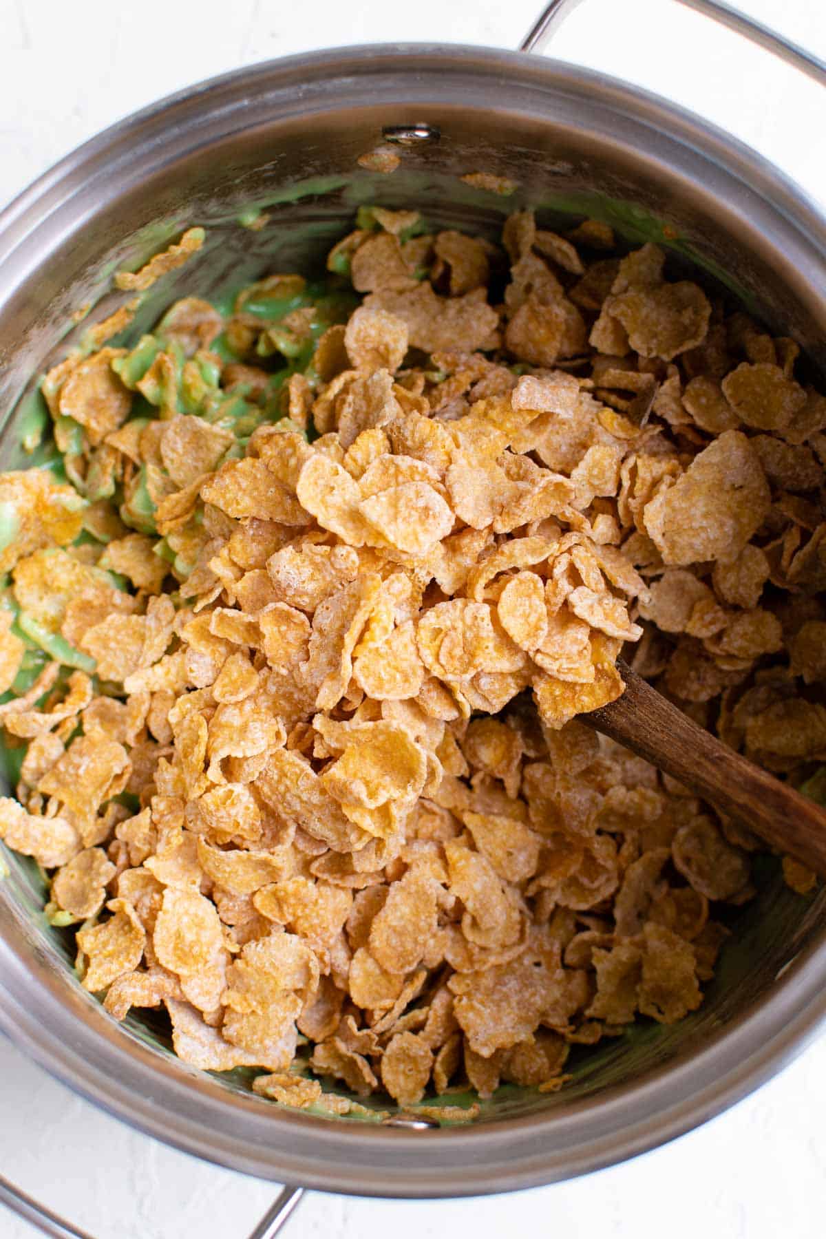 Cornflake cereal is being mixed into the green marshmallow mixture