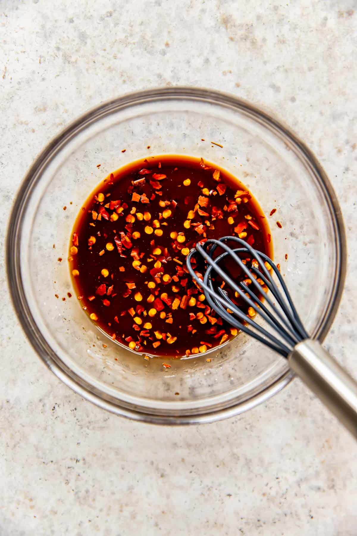 kung pao chicken sauce in a clear bowl with a metal whisk