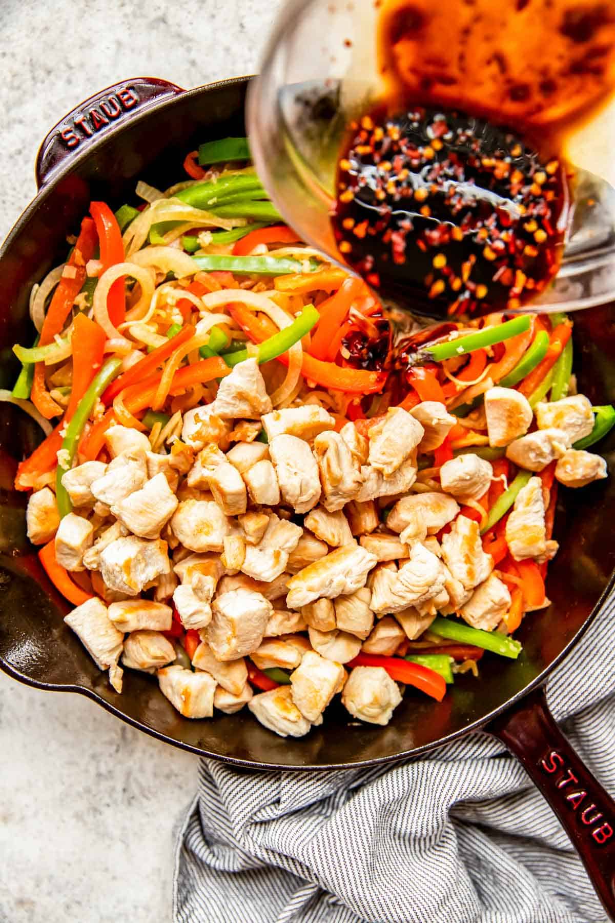 chicken and vegetables in a cast iron skillet with sauce being drizzled on top