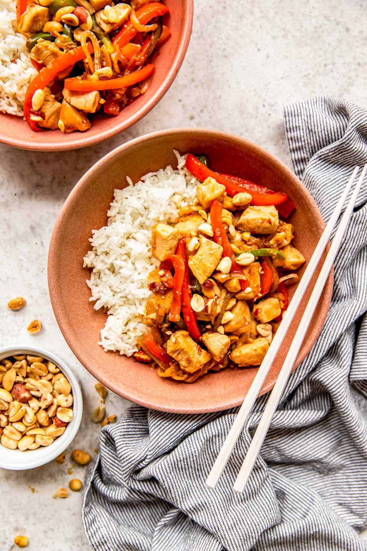 kung pao chicken and rice in a pink bowl with plastic chopsticks on the edge of the bowl