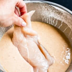 raw chicken breast being dipped into batter in a metal bowl