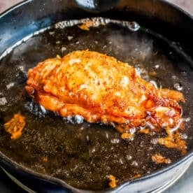 fried chicken breast in bubbling hot oil in a cast iron skillet