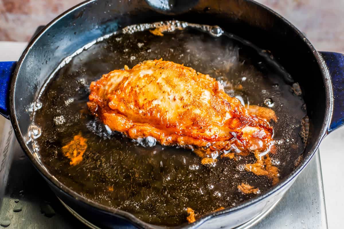 fried chicken breast in bubbling hot oil in a cast iron skillet