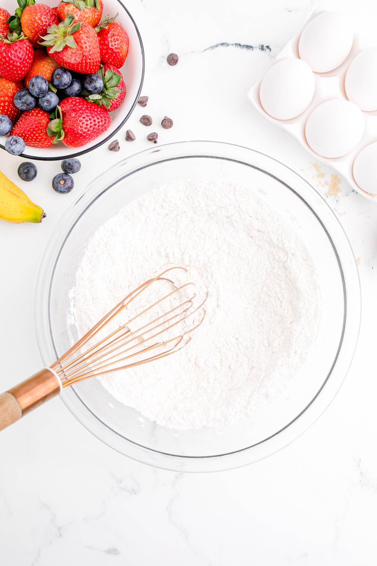 a copper whisk in a clear bowl with flour