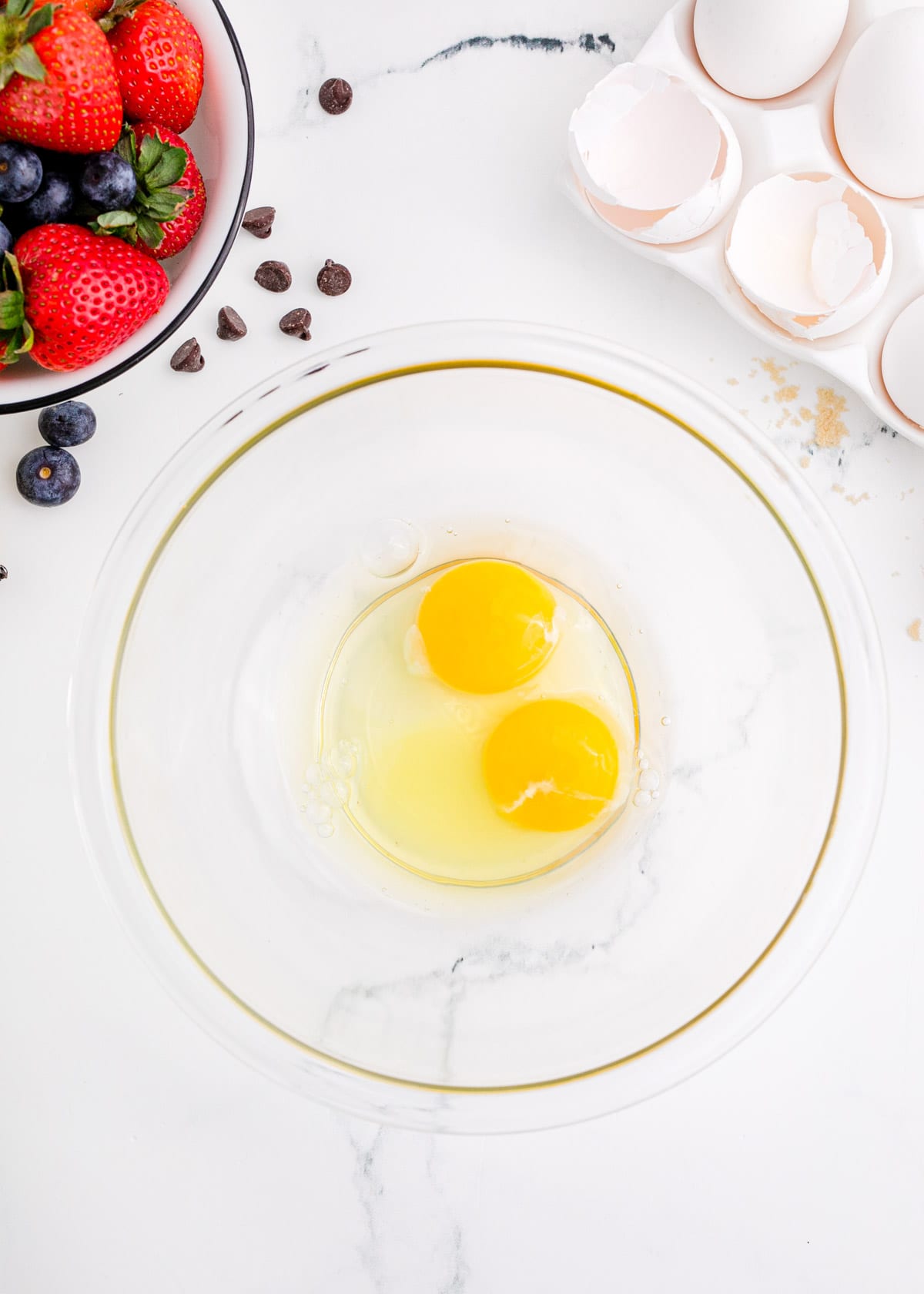 eggs in a clear bowl next to broken egg shells
