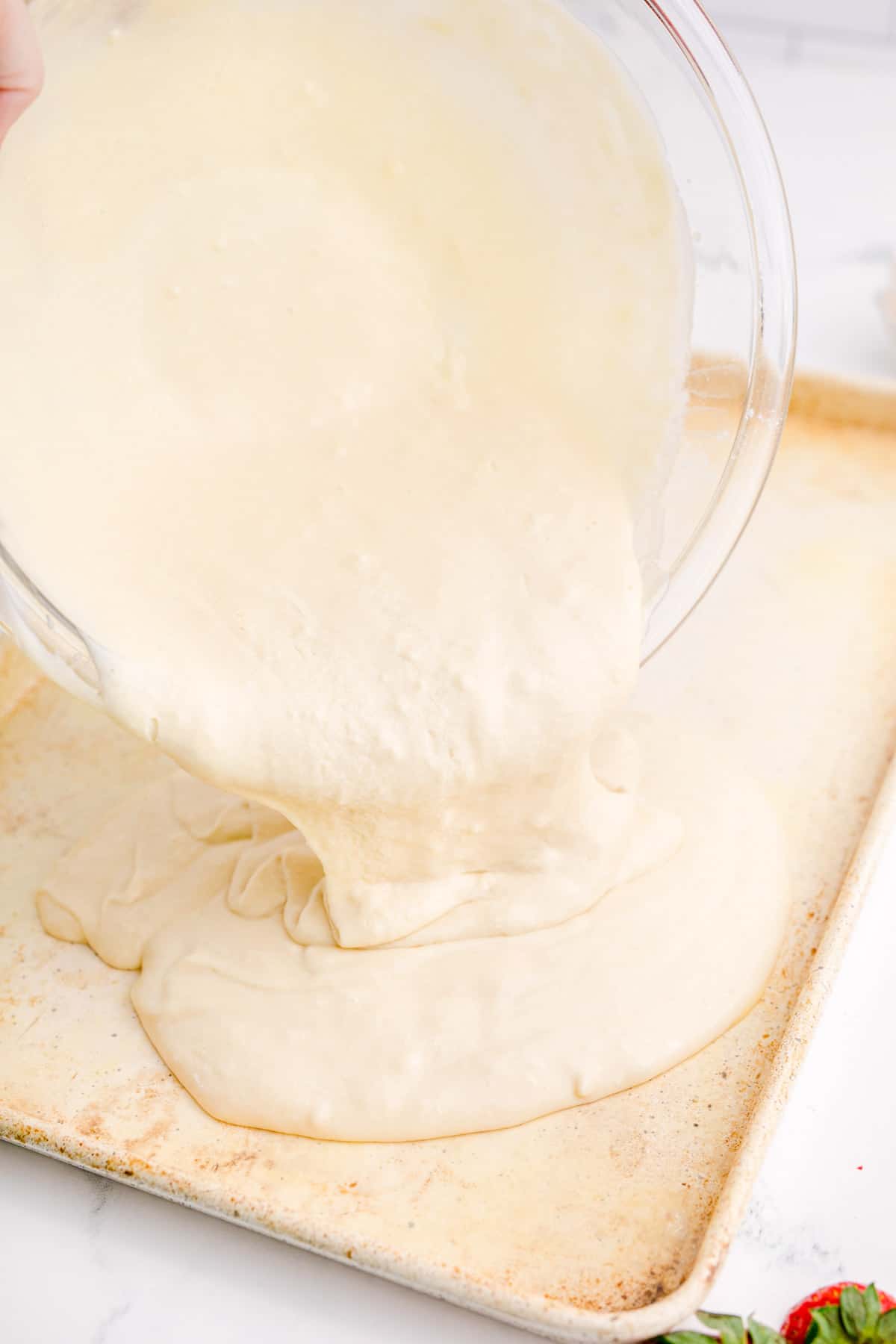 pouring pancake batter from a clear bowl onto a metal sheet pan