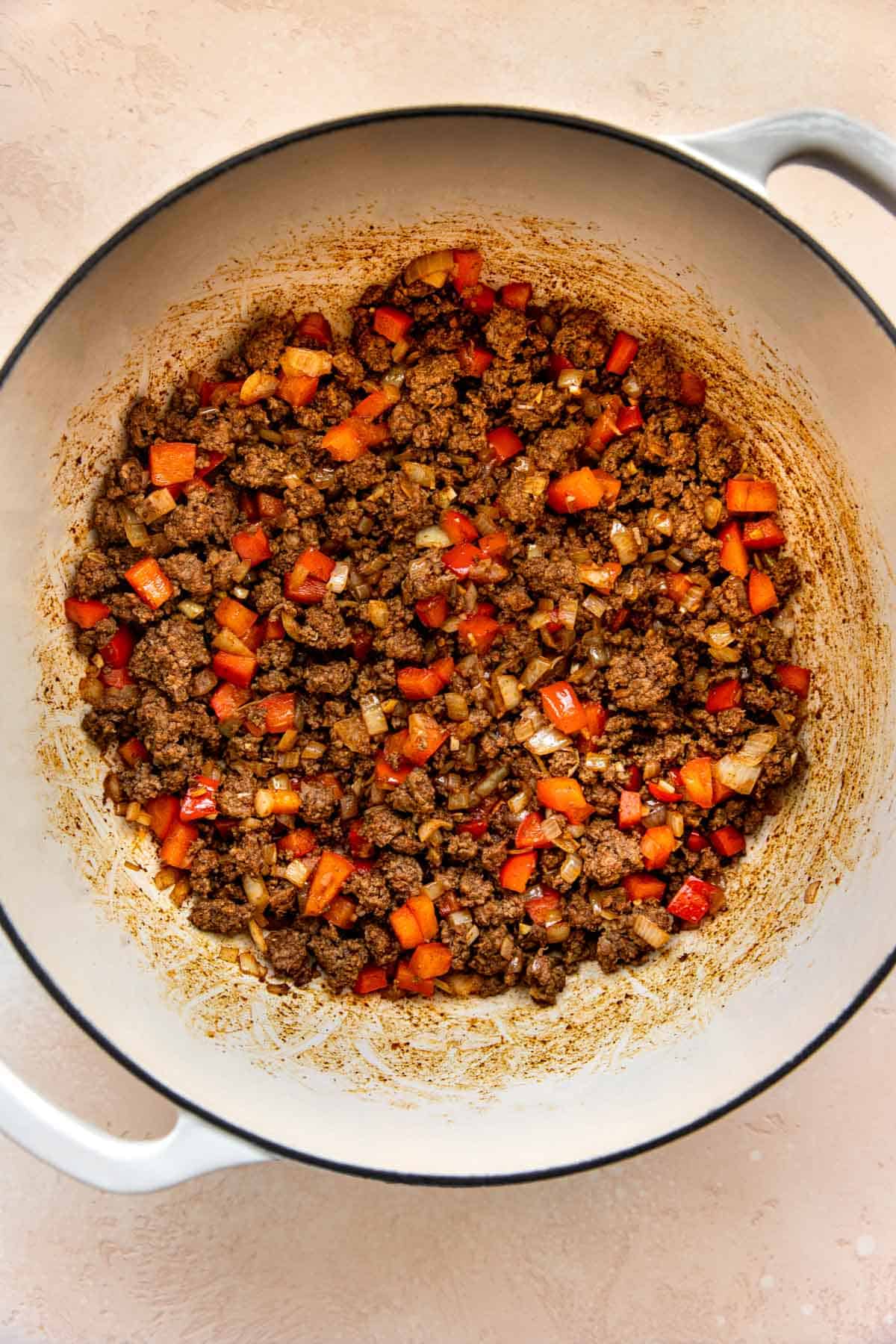 browned ground beef with red bell peppers and onions mixed together in a cast iron skillet