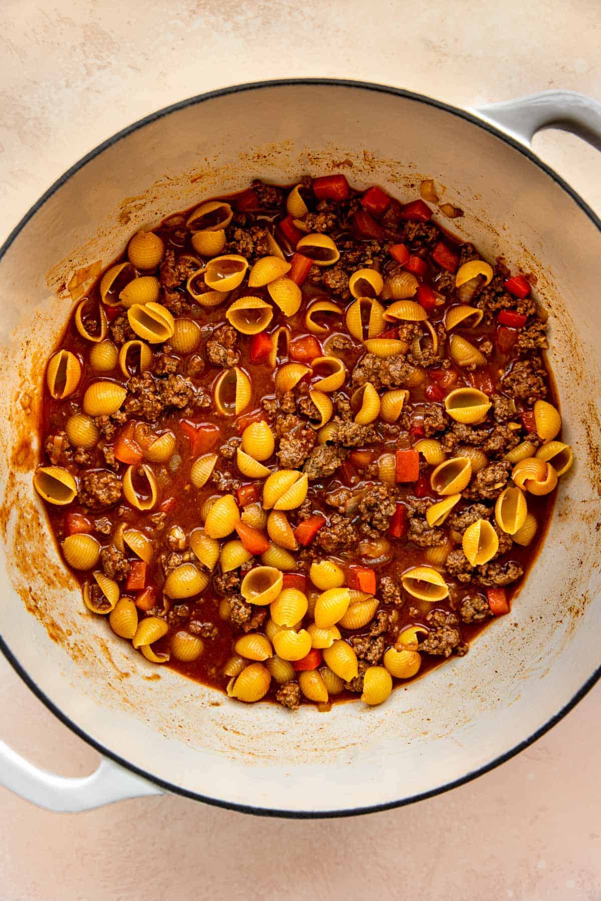 beef broth and dried pasta shells added to the ground beef mixture in the cast iron skillet