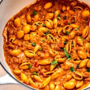 ground beef with pasta shells in a cast iron skillet next to a yellow checkered linen towel with fresh parsley garnished on top