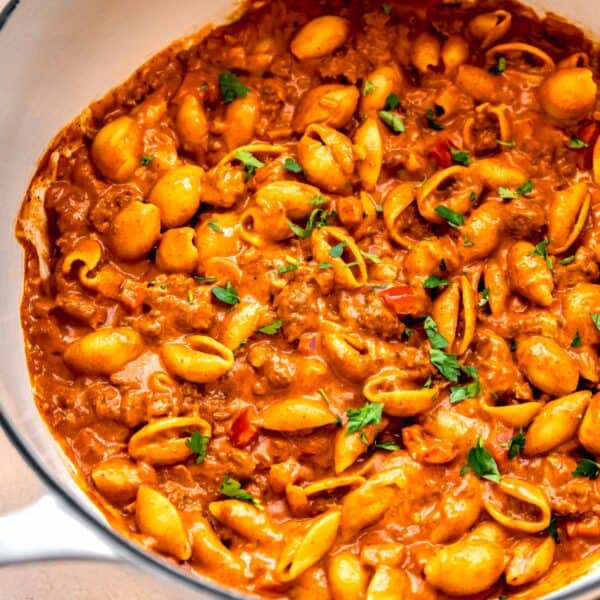 ground beef with pasta shells in a cast iron skillet next to a yellow checkered linen towel with fresh parsley garnished on top