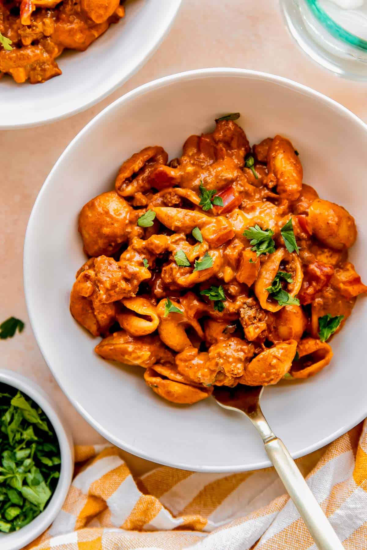 ground beef with pasta shells in a white bowl with a metal fork and garnished with fresh parsley on top