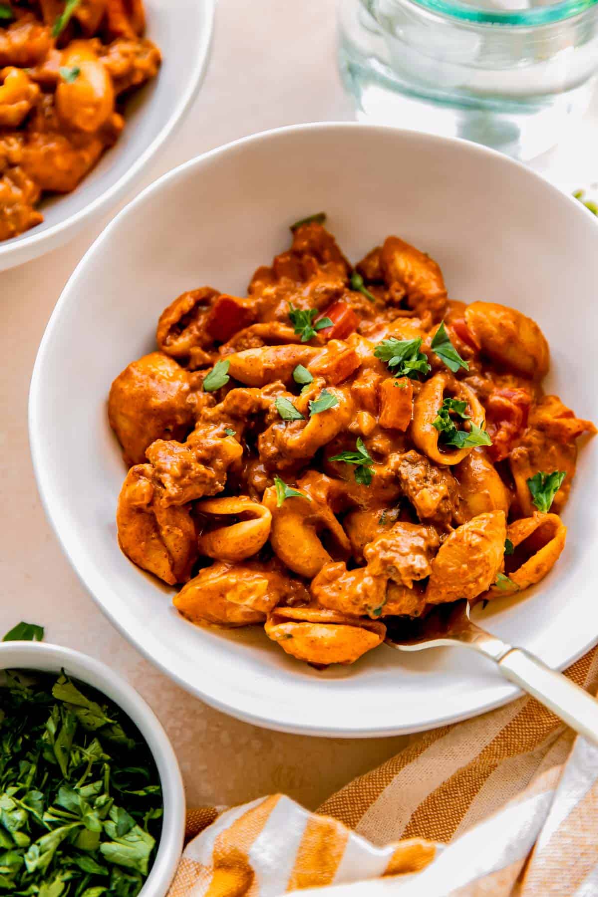 ground beef with pasta shells in a white bowl and a metal fork