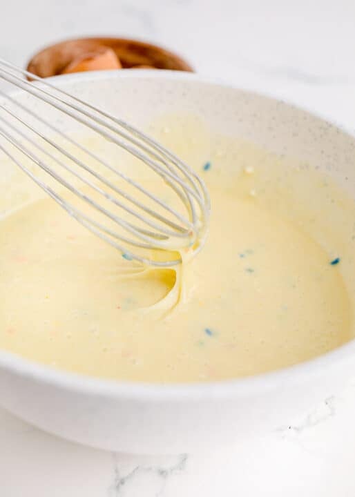 a metal whisk in a speckled bowl with funfetti batter