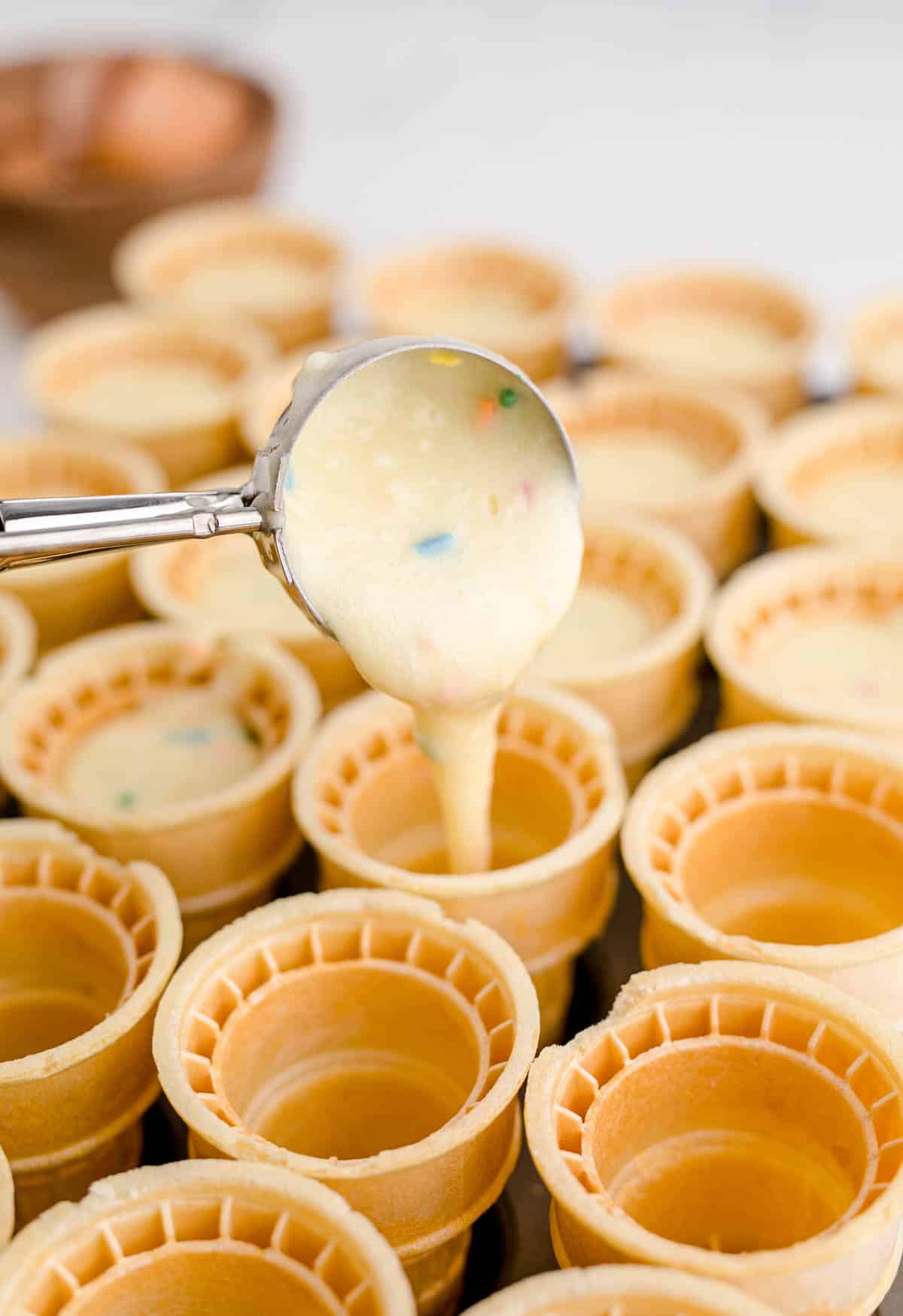 a cookie scoop pouring batter into ice cream cones