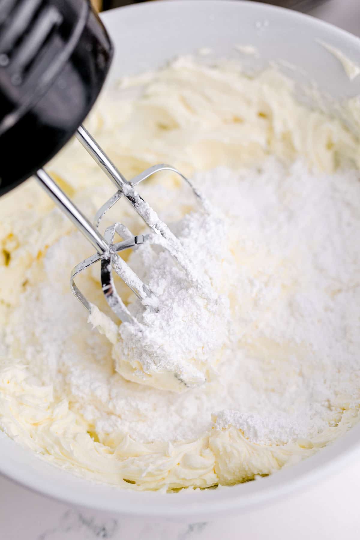 an electric hand mixer is beating powdered sugar and butter