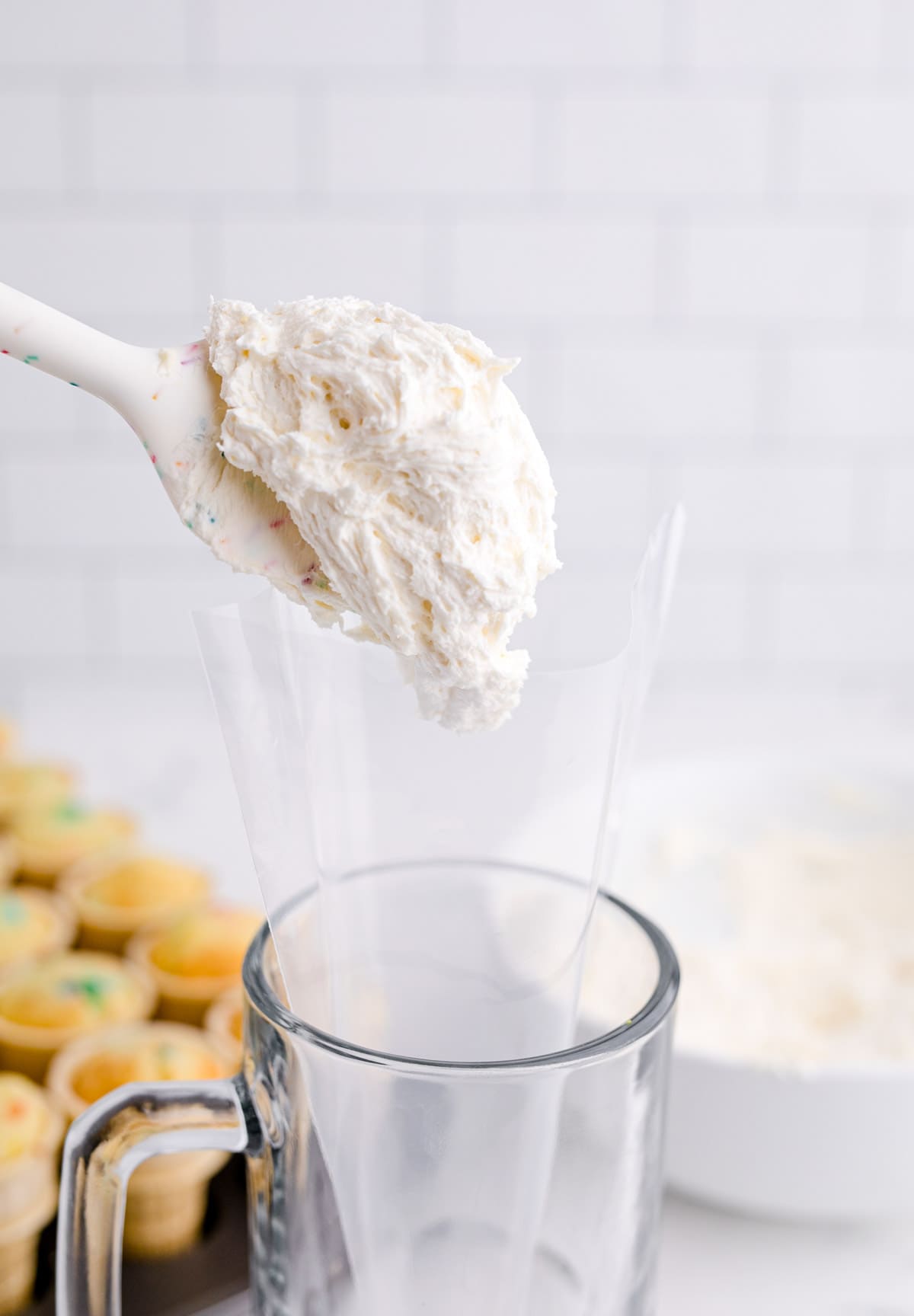 a silicone spatula adding a heaping amount of buttercream into a clear piping bag