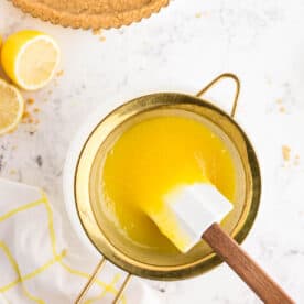 pushing lemon curd through a mesh sieve with a white spatula
