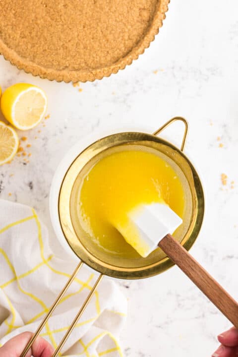 pushing lemon curd through a mesh sieve with a white spatula