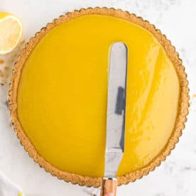 spreading lemon curd mixture into the shortbread crust and tart pan with a metal offset knife